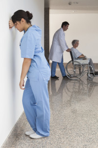 Distressed nurse standing against wall while doctor pushes patient on wheelchair